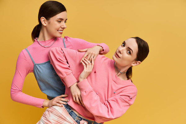 Two beautiful twin sisters showcase their fashion sense with playful poses in a bright setting.