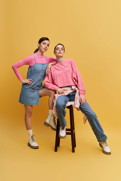 Two lively twin sisters pose against a bright yellow backdrop, showcasing their individuality.