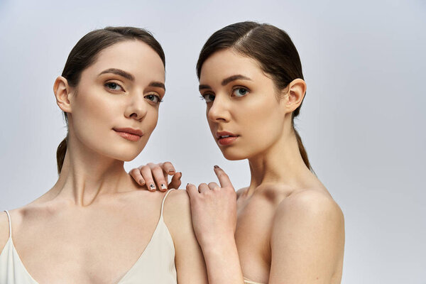 Two sisters stand gracefully together, exuding elegance and charm in a soft lit space.
