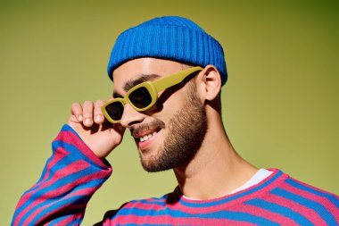 Genç adam eşsiz bir moda anlayışı sergiliyor canlı yeşil bir arka plana karşı şık güneş gözlükleriyle.