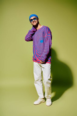 Yakışıklı bir genç, modaya uygun kıyafetlerini ve eşsiz güneş gözlüklerini stüdyo ortamında sergiliyor..