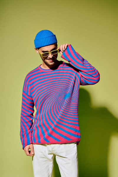 A handsome young man wears a colorful outfit while posing playfully against a green backdrop.
