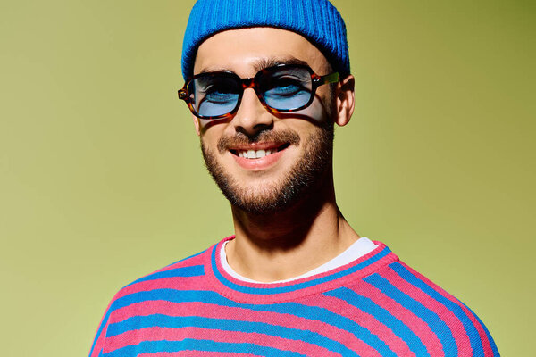 Handsome young man confidently poses in a trendy outfit with vibrant blue sunglasses, exuding style.