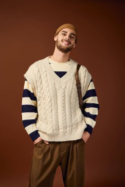 Genç adam benzersiz moda anlayışını kahverengi arka planlı moda stüdyosunda sergiliyor..