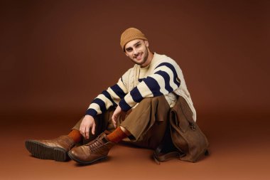 Yakışıklı genç adam, stüdyoda yerde otururken eşsiz moda anlayışını ifade ediyor..