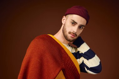 Moda şapkalı genç bir adam, kahverengi bir arka plana karşı moda anlayışını sergiliyor..