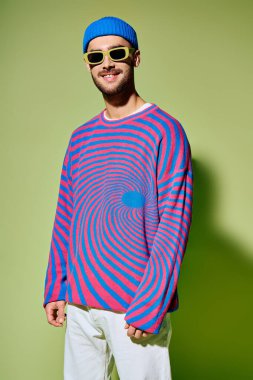 Şık bir genç adam, son moda güneş gözlüğü ve yeşil ışığa karşı parlak bir kıyafetle kendine güvenerek poz veriyor..