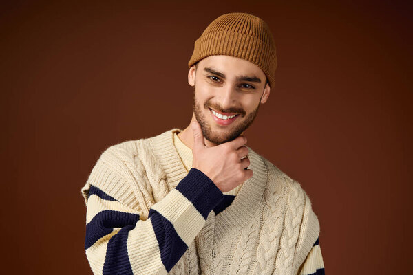Красивый молодой человек уверенно позирует в стильном наряде с модной шапочкой в студии.