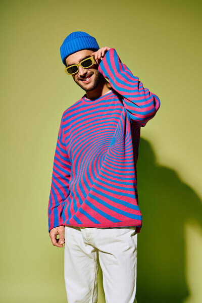 A stylish young man showcases his fashionable outfit against a vibrant green backdrop.