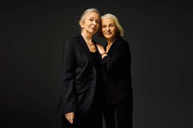 İki şık kadın sıcak bir kucaklaşmayı paylaşıyor. Sofistike kıyafetlere sevgi ve güven yayıyorlar..