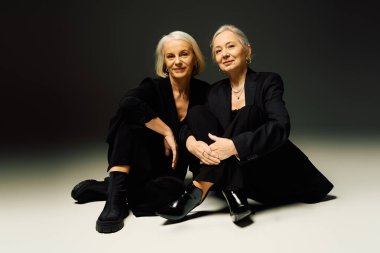 İki modaya uygun kadın yakın otururlar, sıcaklığı ve karşılıklı sevgiyi çağdaş tarzda yayarlar..