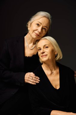 İki olgun kadın özel bir anı paylaşıyor. Şık bir arkaplanda sevgi ve zarafet yayıyorlar..
