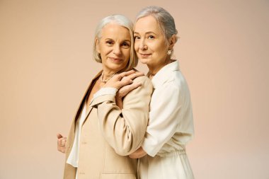 İki zarif olgun kadın, yumuşak bir zemine karşı birbirlerini kucaklarken aynı hassas anı paylaşırlar..