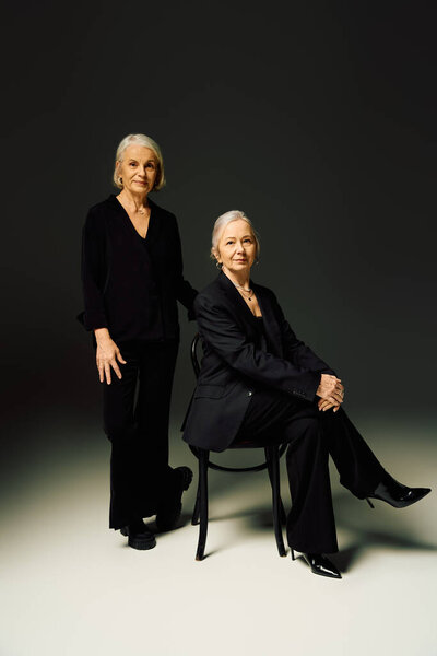 Two stylish mature women stand together in a chic studio, radiating love and confidence.