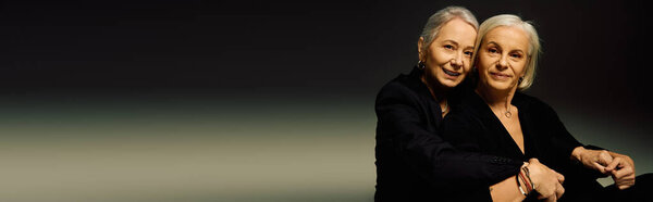 Two fashionable mature women demonstrate affection and style in a modern, elegant environment.