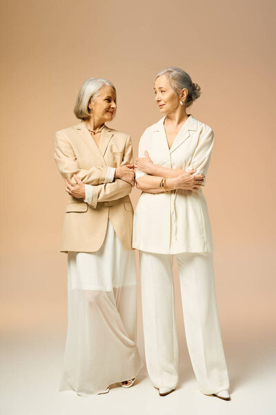 Две модные женщины разделяют теплый момент, излучая любовь и радость в тихом студийном пространстве.