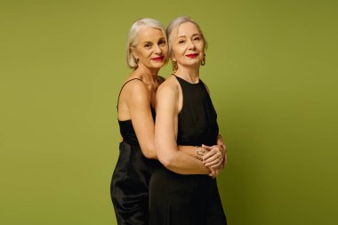 İki olgun kadın, romantik ve şık siyah elbiseler içinde birbirlerine sarılıyorlar..