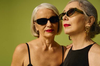 Two mature women express love and elegance, adorned in chic sunglasses against a vivid backdrop. clipart