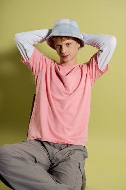 Genç bir adam şık bir elbise ve modaya uygun bir şapka sergileyerek rahat bir şekilde oturuyor..