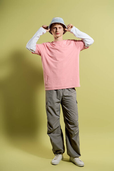 A young man sports a trendy light pink shirt and bucket hat against a vibrant backdrop.