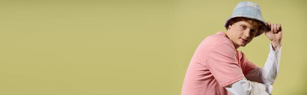 A young handsome man showcases his trendy style, leaning casually in a vibrant setting.