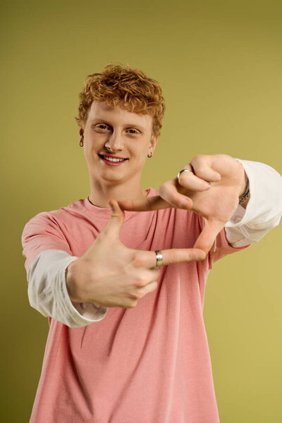 Стильный молодой человек улыбается и создает рамку руками, наслаждаясь моментом в помещении.