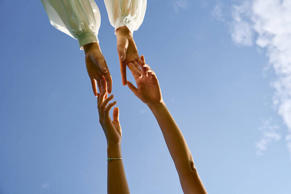 Two graceful hands reach for each other against a clear blue sky, symbolizing connection.