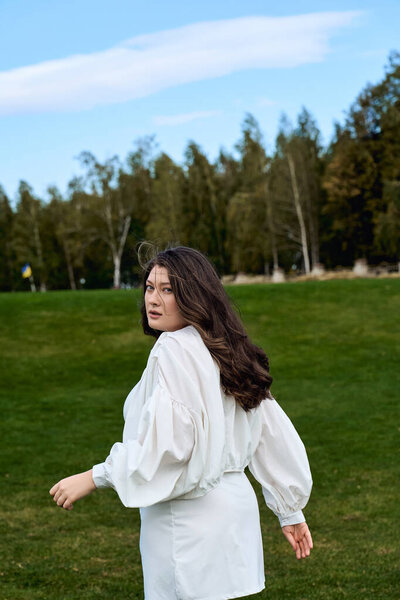 Confident young woman walks through a vibrant park, enjoying nature and spring fashion.
