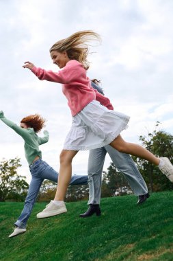 Üç modaya uygun arkadaş yeşil park alanında koşan kendine güvenen bir bahar gününün tadını çıkarıyor..