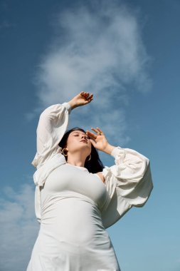 Havalı bir kadın, çarpıcı bir arkaplan karşısında zarifçe poz verirken açık havaya sarılır..