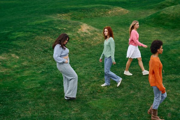 Stylish ladies walk gracefully across lush green grass, enjoying the beauty of spring outdoors.