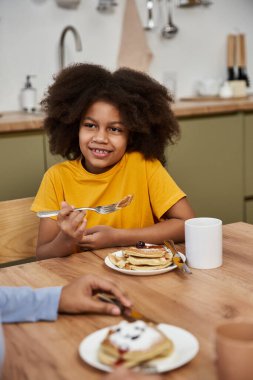 Genç bir kız, annesiyle kahvaltı ederken gülümsüyor..