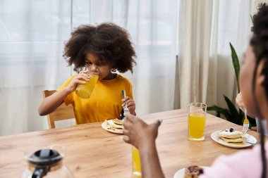 Genç bir kız kahvaltı masasında ailesiyle krep paylaşırken meyve suyu içer..
