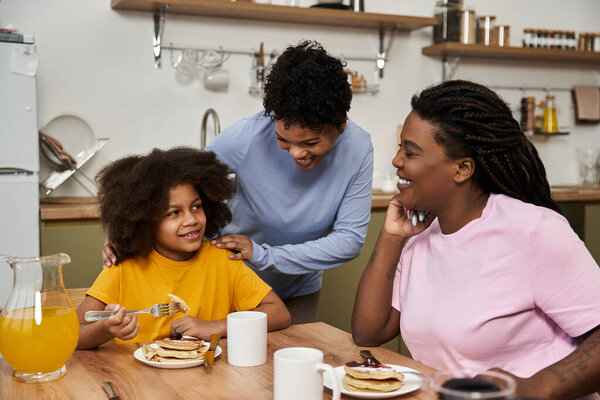Любящая семья делится смехом и блинами за уютным завтраком, создавая заветные воспоминания.