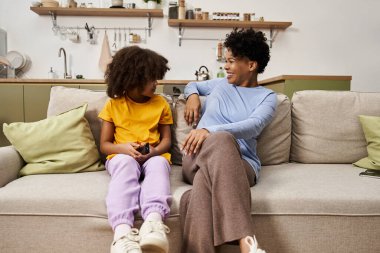 Sıcak bir oturma odasında, bir anne ve kızı neşeli bir kahkahayı paylaşıyor, birlikte eğleniyorlar..