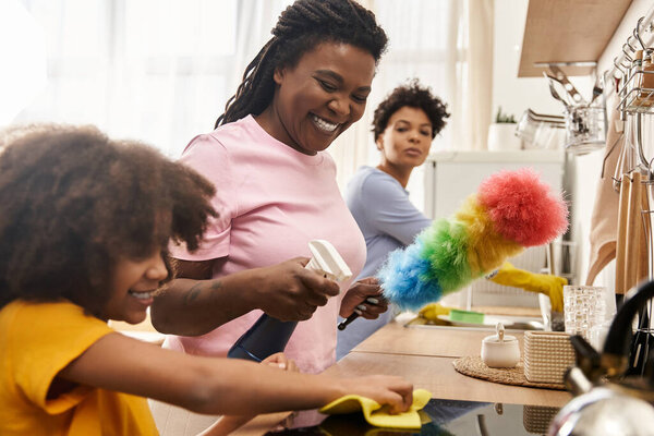 Daughter helps her moms clean the kitchen, sharing laughter and bonding during chores at home.