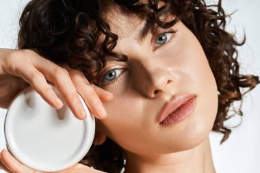 Güzel bukleli genç bir kadın nazikçe yüzüne yakın bir teneke kutu tutuyor, sıcaklığını yayıyor..