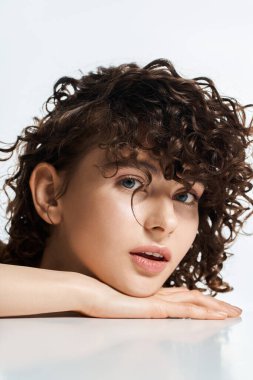 Kıvırcık saçlı, güzel bir kadın çenesini ellerine dayamış, büyüleyici bir şekilde..