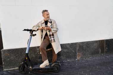 Moda kıyafetleri içinde son sınıf öğrencisi telefonunu kontrol ederken elektrikli scooter 'a yaslanıyor..