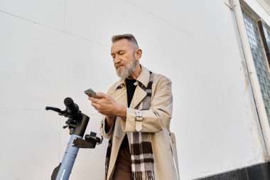 Şık bir ceket ve eşarp giyen son sınıf öğrencisi scooterın yanında dururken akıllı telefonunu kontrol ediyor..