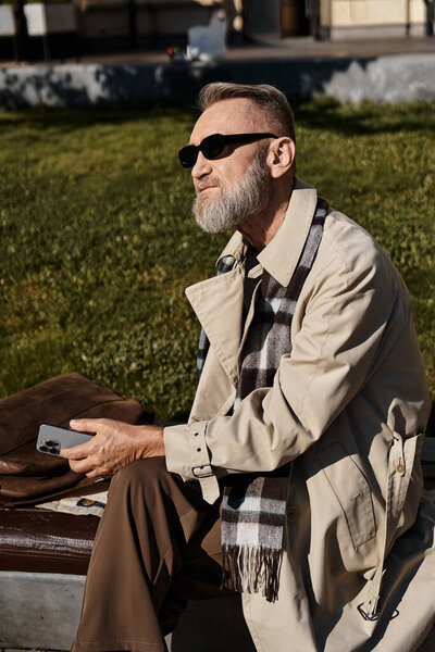 A sophisticated senior man sits casually on a park bench, dressed in chic clothing.