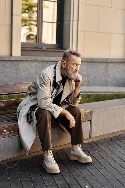 A debonair senior man sits thoughtfully on a city bench, clad in fashionable clothing.