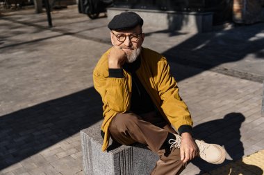 Şık, son sınıf öğrencisi bir adam bir şehir bloğunda oturuyor, büyüleyici bir gülümsemeyle dizlerine yaslanıyor..