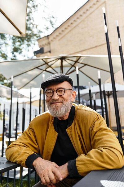 Даппер-старший со стильной бородой и круглыми очками расслабляется на улице в модном кафе.
