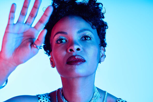 A stylish woman with curly hair captivates with her striking presence in blue light.