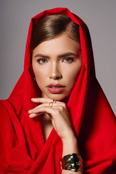 A chic young woman with striking eyes poses elegantly in a flowing red shawl.
