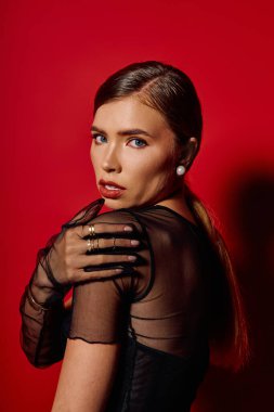 Genç, zarif bir kadın şık tarzını canlı kırmızı bir arka plana karşı özgüvenle sergiliyor..