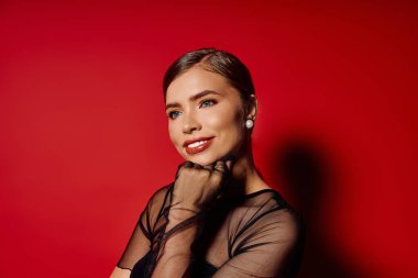 Şık bir kadın kendine güvenerek kırmızı arka plana karşı gülümsüyor, zarafetini sergiliyor..