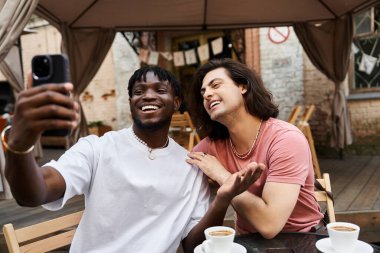 İki yakışıklı, açık bir kafede selfie çekerken kahkahalarını paylaşıyor..