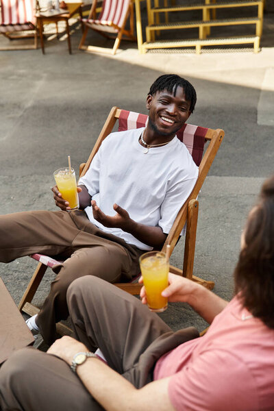 Два красивых мужчины наслаждаются выпивкой, смеясь и улыбаясь в уютном кафе в солнечный день.